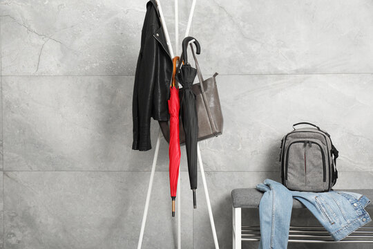 Colorful umbrellas, jacket and bag on clothing rack near gray marble wall