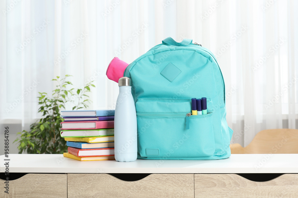 Poster backpack with different school stationery and bottle on desk in room