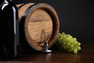 Corkscrew with metal handle, grapes, bottle of wine and barrel on wooden table