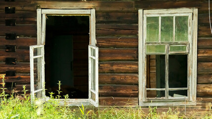 broken windows of an abandoned village house overgrown with grass