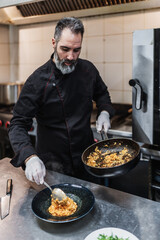 Handsome bearded professional chef works in restaurant kitchen. He prepares healthy delicious dish with fish and seafood.