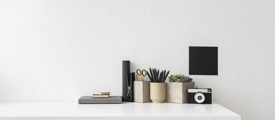 Creative desk with an empty space, desk objects, office supplies, books, and plant on white wall...
