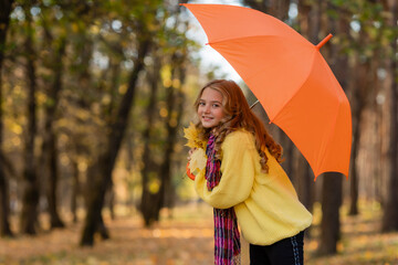  little blonde girl walks in the park in autumn with an orange umbrella