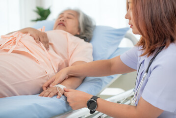 Asian female nurse gives saline solution to senior woman patient