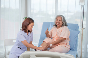 Obraz premium Asian female nurse bandaging foot of elderly woman patient