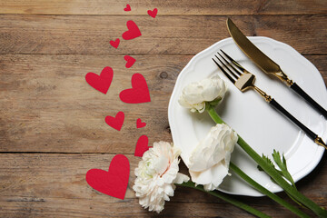 Table setting for romantic Valentine's day celebration, top view. Plate, cutlery, flowers and hearts on wooden table, space for text
