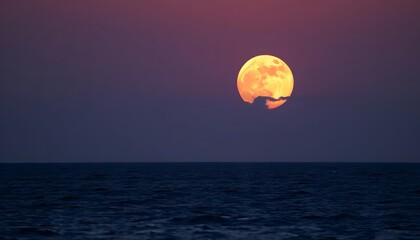 A full moon rising over a dark ocean at sunset, with an orange and red sky in the background