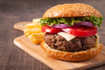 Homemade delicious hamburger with beef, onion, tomato, lettuce and cheese. Fresh burger close up on wooden rustic table with potato fries. Cheeseburger. Burger.
