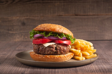 Homemade delicious hamburger with beef, onion, tomato, lettuce and cheese. Fresh burger close up on wooden rustic table with potato fries. Cheeseburger. Burger.