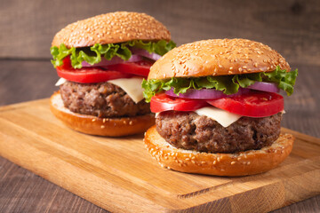 Homemade delicious hamburger with beef, onion, tomato, lettuce and cheese. Fresh burger close up on wooden rustic table with potato fries. Cheeseburger. Burger.