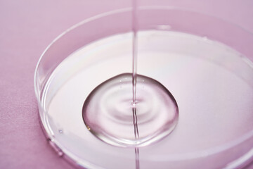 Serum or cosmetic oil flows into a transparent bowl on a purple background.
