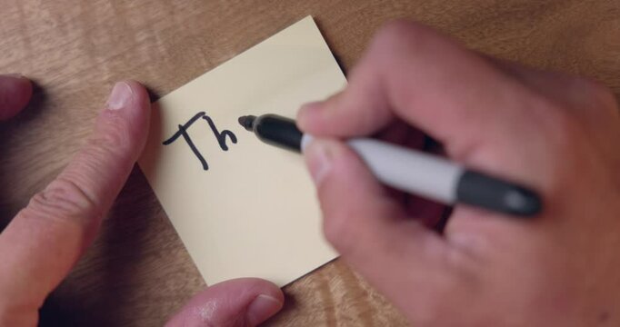 A person is writing on a sticky note on a desk background. the person is writing Thank you video is in 30 fps
