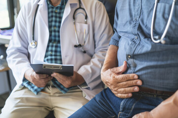 A doctor is examining an elderly man with stomach pain in the medical room, holding his belly. Portrait of senior man sharing health issues struggles with his medical professional carer practitioner