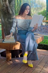 Woman Reading Books Outdoors on a Wooden Bench