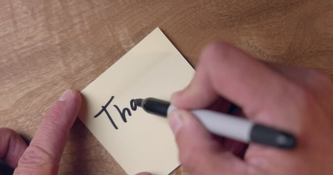 A person is writing on a sticky note on a desk background. the person is writing Thank you video is in 60 fps