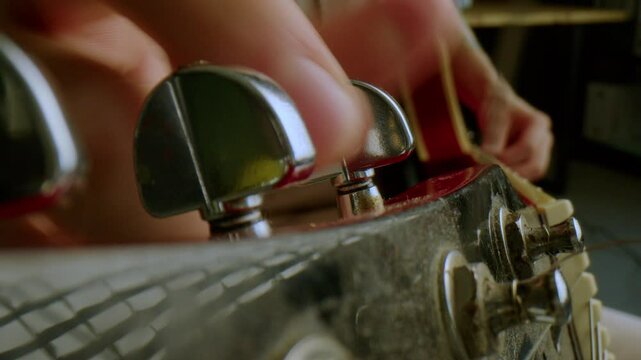 Hand of male musician using tuning pegs while adjusting guitar strings before playing. Extreme close-up view