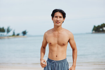 Happy Asian Man Enjoying Summer Vacation on Tropical Beach, Smiling with Muscular Torso and Sexy Abs, Relaxing in the Sun on Sandy Island