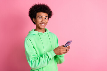 Photo of nice young man use phone empty space wear green hoodie isolated on pink color background