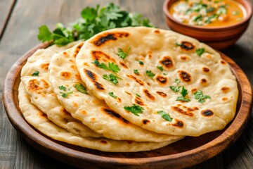 Stack of fresh chapati garnished with herbs, served with curry in a traditional wooden platter