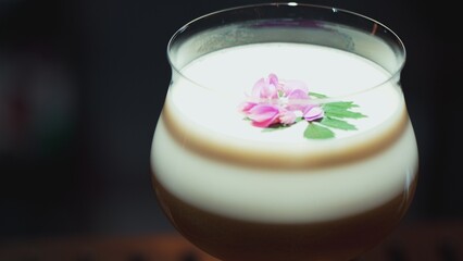 Closeup rotating in passion fruit smoothy cocktail glass serving special refreshing drink garnished with pink flower on smooth fizzy in showcasing nightlife mixology at luxurious nightclub. Vinosity.