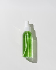 Transparent spray bottle with green liquid. Skincare essentials, spa beauty product isolated on white background, Cosmetic packaging with serum or lotion at sunlight, minimal top view object