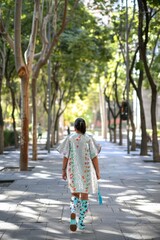 Woman in Sparkling Jacket Walking Through a Tree-Lined City Park on a Sunny Day