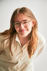 Fototapeta premium Portrait of beautiful girl smiling to camera. Cute girl in cream shirt and square glasses posing on white background.