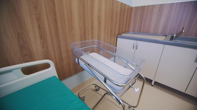 Bed and crib near sink with baby changing table in empty ward. Hospital room equipped for mother and newborn baby for comfortable stay