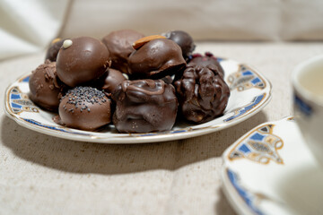 Assorted chocolate truffles on a plate accompanied by a cup of red tea.