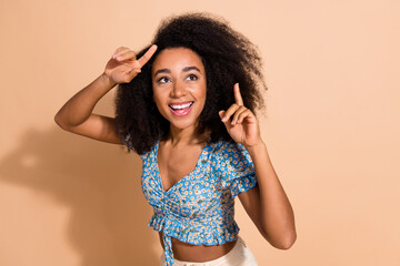 Photo of adorable lovely girl wear blue top pointing two fingers looking empty space isolated beige color background