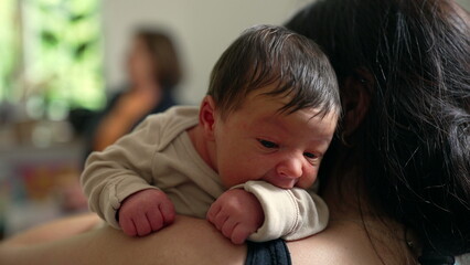 Obraz premium Newborn baby on parent's shoulder, gazing curiously. The intimate moment is filled with love and warmth, capturing the bond and security the baby feels in the parent's arms