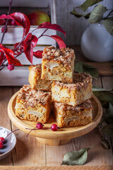Slices of Dutch apple cake with streusel on a wooden tray, apples and apple branches on a wooden background.
