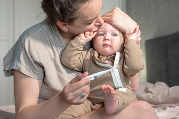 Mom measures body temperature baby by electronic thermometer. Sick child with high temperature. Children illness, clod and flue, runny nose, cough, disease, parent care