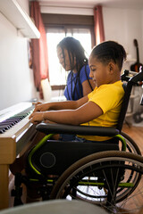 Vertical shot of two dark-skinned brothers playing an electronic piano in their living room. The disabled child in a wheelchair is in the foreground. Concept of young African people playing a piano. ©  Yistocking