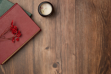Books with flowers and candle on wooden background from above. Flat lay, top view.