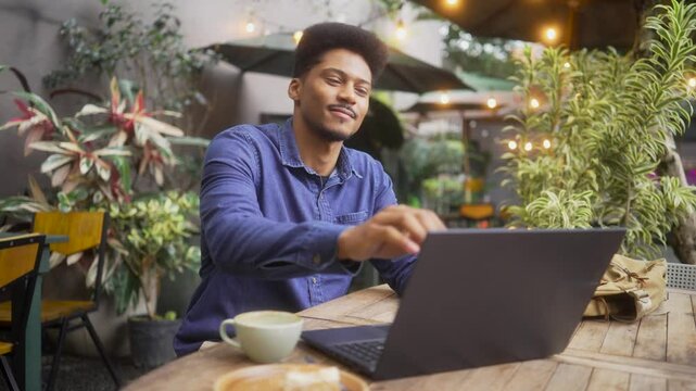 Relaxed young professional or university student closing laptop after completing work in an outdoor cafe. Satisfied with his work, routine, he prepares to pack up and leave the cozy setting