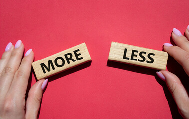 More or Less symbol. Concept word More or Less on wooden blocks. Businessman hand. Beautiful red background. Business and More or Less concept. Copy space