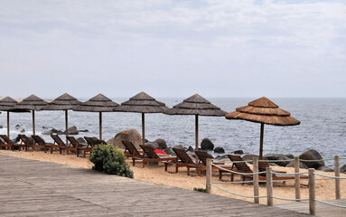 Morning on a beach on a less hot day with cloudy skies and straw umbrellas