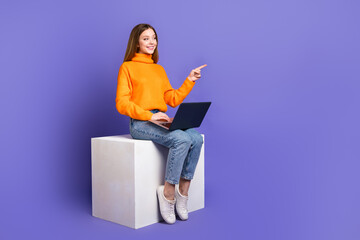 Photo of teen girl in orange turtleneck and jeans using laptop pointing finger her first website mockup isolated on purple color background