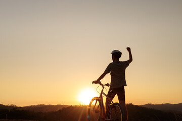Obraz premium Mountain biker takes a break at sunset, raising an arm in celebration. The stunning sunset and peaceful atmosphere evoke a sense of achievement, freedom, and passion for outdoor adventure