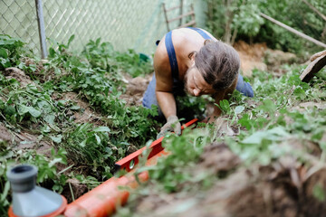 A male plumber installs a sewer pipe in the yard of a house.