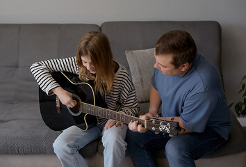 Happy dad teaches his kids to play the guitar while sitting on the sofa in the living room at home. Happy Father's Day.