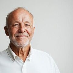 Fototapeta premium A happy senior man in his mid-60s wearing white shirt, smiling softly against a clean light grey background