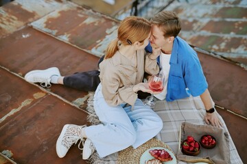 Couple sharing intimate moment during rooftop picnic at sunset. They enjoy fresh fruit and drinks...