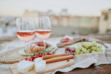 Charming rooftop picnic setup featuring rose wine glasses, cheese, grapes, croissant, and assorted snacks creating a relaxing ambiance for outdoor dining enjoyment