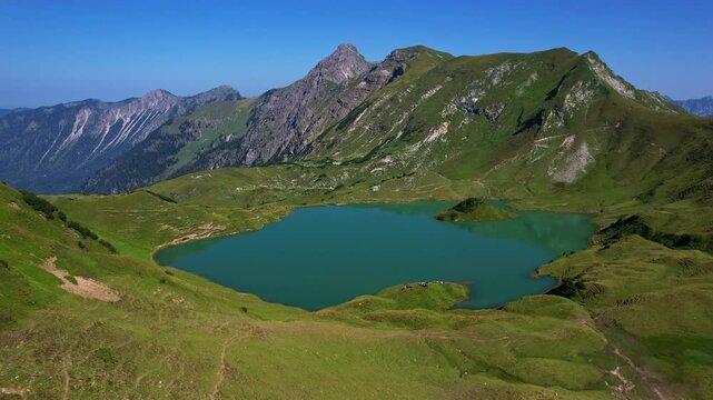 4K Aerial Drone video of the most beautiful mountain lake Schrecksee in Bavarian Alps with the cows feeding on lush green grass on a sunny day with blue skies and rocky hill tops surrounding