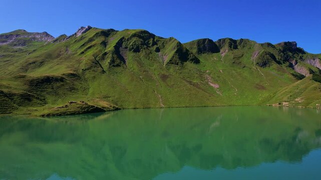 4K Aerial Drone video of the most beautiful mountain lake Schrecksee in Bavarian Alps with the cows feeding on lush green grass on a sunny day with blue skies and rocky hill tops surrounding
