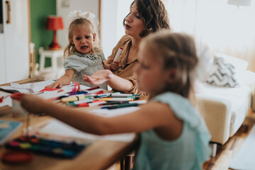 A mother and her two daughters enjoy a creative arts and crafts session at home. The scene captures...