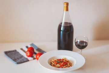 Italian pasta with tomatoes and basil, bottle of red wine and glass. Spaghetti. National cuisine Recipe Rustic. A classic Italian pasta dish with tomato sauce and basil at the table.