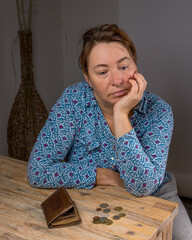 Woman sitting at  desk at home. In front of her lies an empty wallet and some coins.  Poor person...
